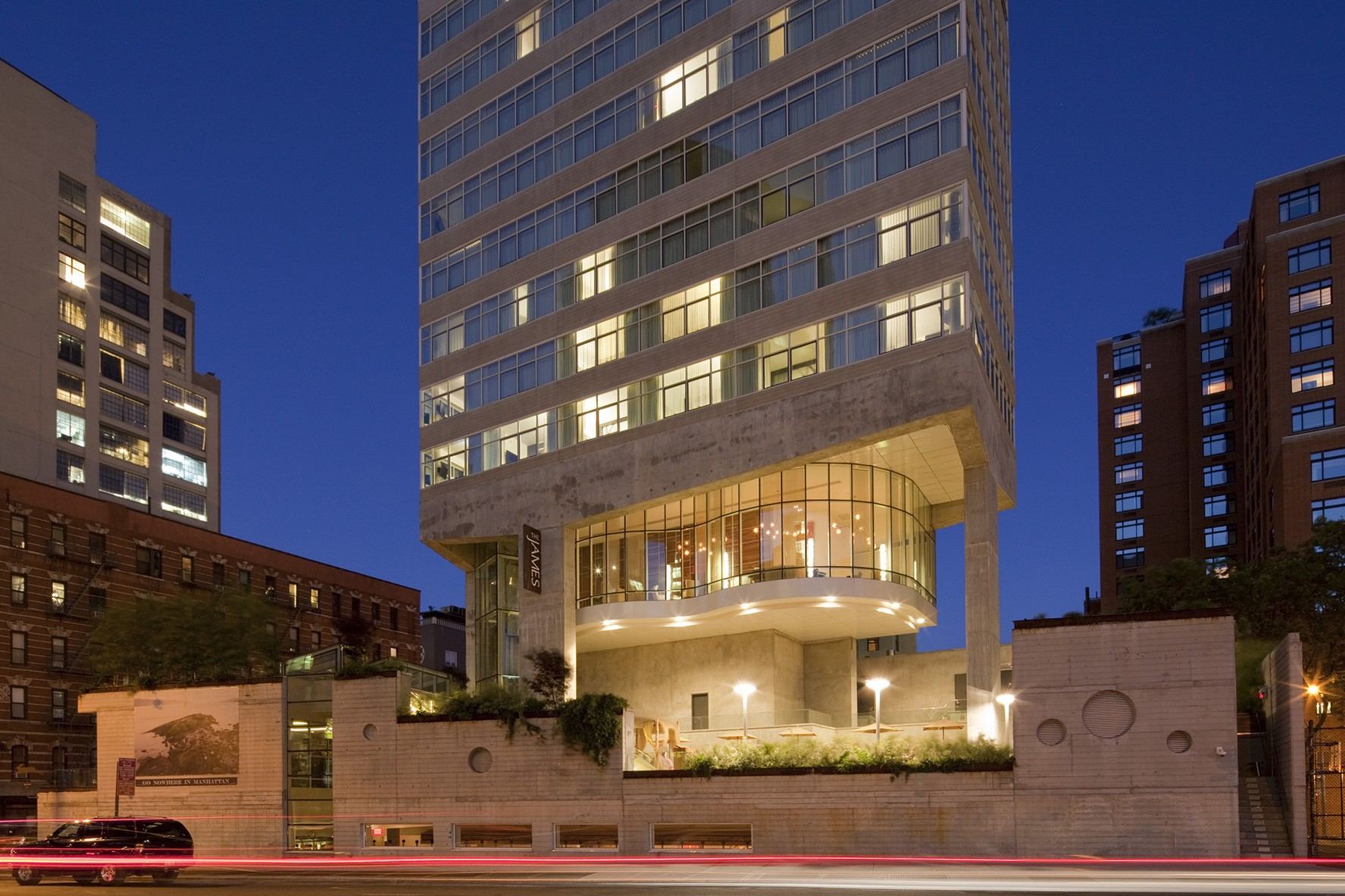 The James New York at dusk, its glass lounge lit above the street